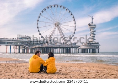 couple on the beach of Scheveningen Netherlands during Spring, The Ferris Wheel at The Pier at Scheveningen in the Netherlands, Sunny spring day at the beach of Holland Royalty-Free Stock Photo #2243700411