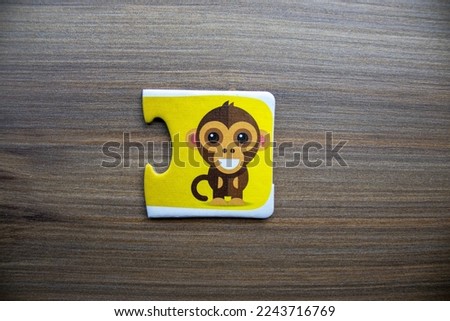 Yellow knowledge puzzle with a picture of a laughing monkey placed on a wooden background.