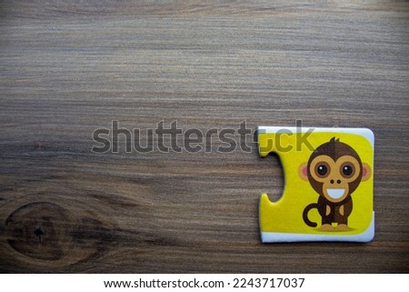 Yellow knowledge puzzle with a picture of a laughing monkey placed on the right of a wooden background.