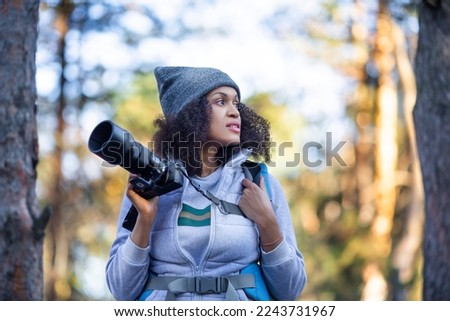 African American woman walking in the forest with a camera looking by side. Close up photo.