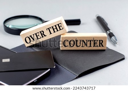 OVER THE COUNTER text on a wooden block on black notebook , business concept