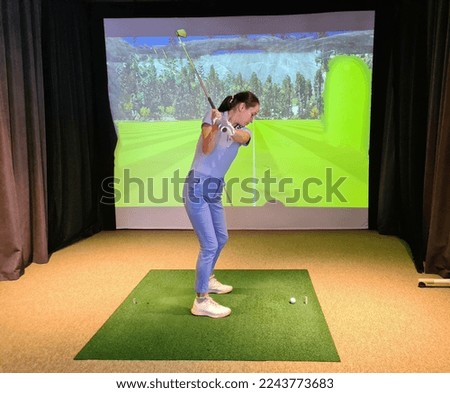 Girl playing golf on screen and golf simulator. Young golfer playing golf video game indoors