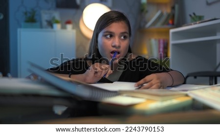 Young focused school, college girl with pen in mouth think worried  doing assignment project homework for exams. Hard working Indian teen concentrating on study that does not know the answer solution Royalty-Free Stock Photo #2243790153