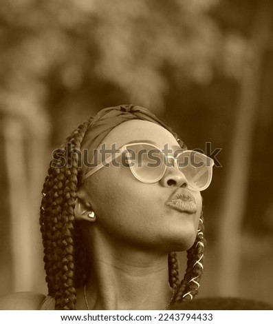Portrait of a young African woman with dreadlocked pigtails on her head. A young adult girl from Africa in sunglasses in nature.