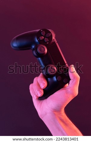 A hand holding a game console controller on a colorful background,red and blue lights,Online gamer concept.