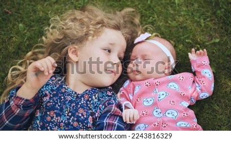 A little girl kisses her baby sister in the garden on the grass.