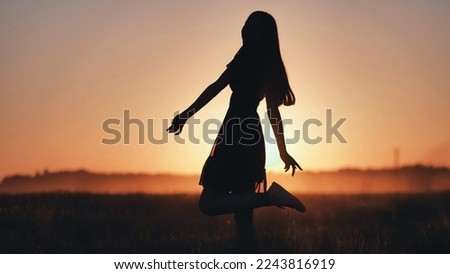 A silhouette of a young girl dancing and spinning on a warm summer evening at sunset.