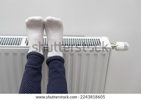 Woman warming up with feet on heater Winter socks drying on a heater