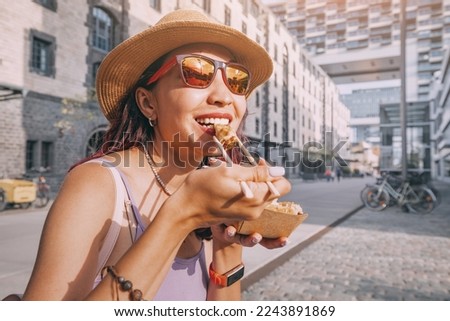 Happy cheerful girl eating spring rolls from takeaway paper box using chopsticks at Cologne city street. Fast food eatery and asian cuisine Royalty-Free Stock Photo #2243891869
