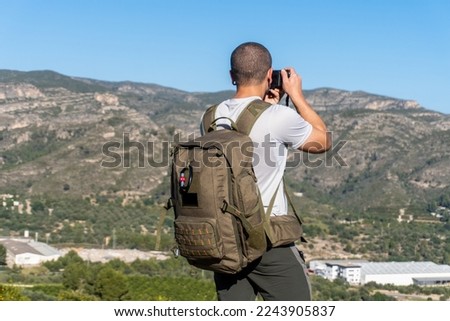 Man with backpack photographs the landscape on a clear sunny day.