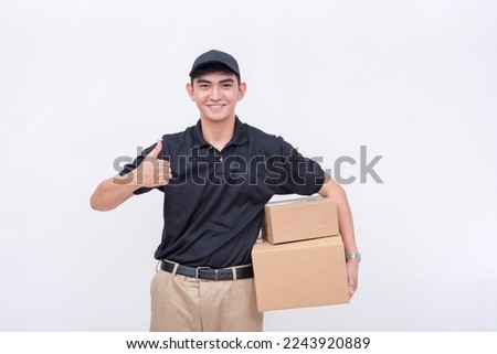 A handsome asian delivery man, carrying two boxes while making a thumbs up sign. Concept of quick and reliable logistics. Isolated on a white background.