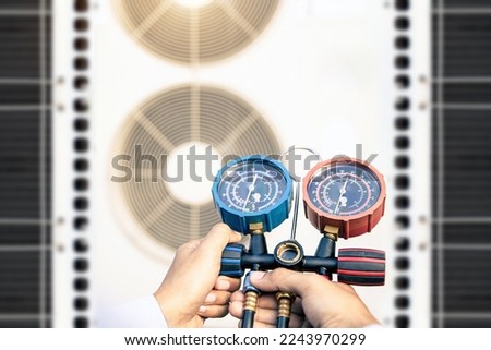 Heat and Air Conditioning, HVAC system service technician using measuring manifold gauge checking refrigerant and filling industrial air conditioner after duct cleaning maintenance outdoor compressor. Royalty-Free Stock Photo #2243970299