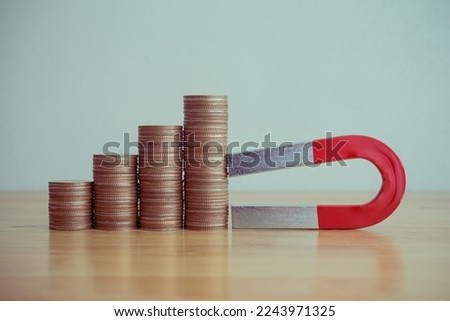 Magnet is attracting stacks coins as growth capital gains graph chart on wooden table white wall background copy space. Investment in stock market, funds, forex, etc. concept. Investor finds best gain