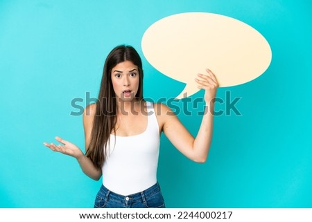 Young Brazilian woman isolated on blue background holding an empty speech bubble with surprised expression