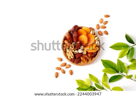 Dried fruits and nuts mixed in a wicker plate, branch with young green leaves. Concept of the Jewish holiday Tu Bishvat on white background with copy space Royalty-Free Stock Photo #2244003947