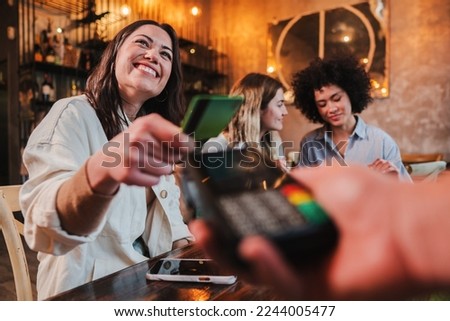 Happy young woman paying bill with a contactless credit card in a restaurant. Female smiling holding a creditcard and giving a payment transaction to the cashier. High quality photo Royalty-Free Stock Photo #2244005477