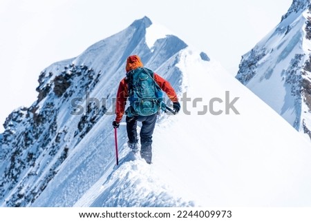 Mountain climber on a steep narrow snow ridge, extreme alpinist mountaineer, Monch, Bernese Alps, Swiss Royalty-Free Stock Photo #2244009973