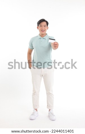 Full body length photo of a standing cheerful young handsome man, holding a credit card, paying online for the bills, isolated on white background