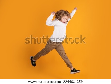 Full length of excited kid jumping. Full body of little child jump wear casual t-shirt and jeans isolated on yellow background.
