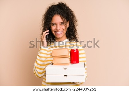 Young african american woman holding a pizza and burger fast food calling with mobile phone isolated