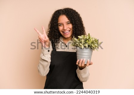 Young african american gardener woman holding a plant isolated joyful and carefree showing a peace symbol with fingers.