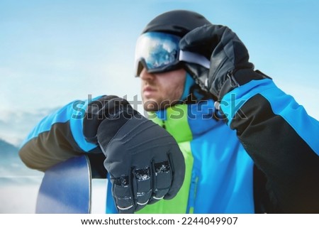 Close Up Of The Ski Goggles Of A Man With The Reflection Of Snowed Mountains. Man In The Background Blue Sky.  Winter Sports.