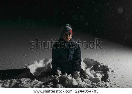 A little boy is playing in the deep snow in the evening