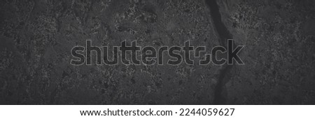 Texture of old cracked concrete wall. Rough faded dark gray concrete surface with spots, cracks, noise and grain. Dark wide panoramic background for grunge style design. Shaded texture with vignette.