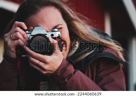 Blond woman takes a photo. Girl with long fair hair focuses with an analog camera. Inspiring young creative artist making photo with vintage retro camera.
