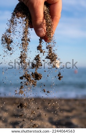 a hand drops sand with the sea with waves and the sand of the beach in a blurred background