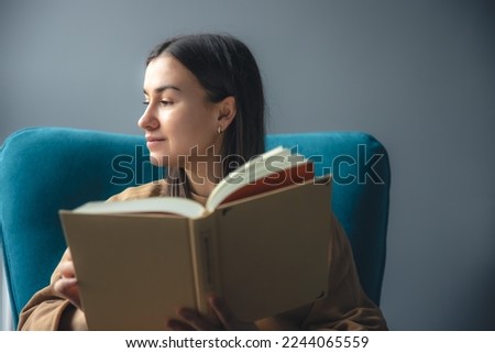 A young woman is reading a book while sitting in a chair.
