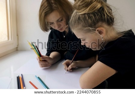 A happy family. Mom and daughter are painting together, sitting by the window.