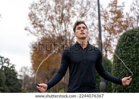 Concentrated guy with curly hair training with jumping rope during fitness workout in blurred park