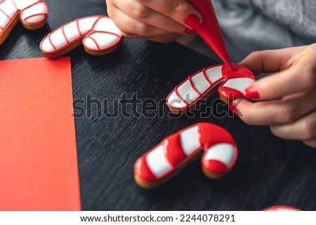 A woman covers with icing Christmas gingerbread in the form of a candy.