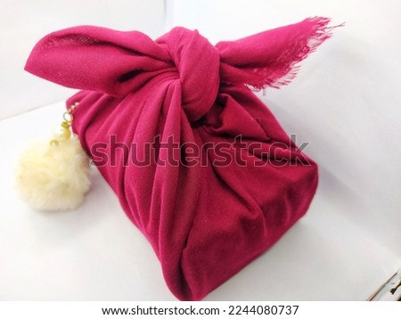 A gift wrapped in a red cloth.  Adorned with a white fluffy ball hanger.  Birthday gifts.  Isolated on a white background.