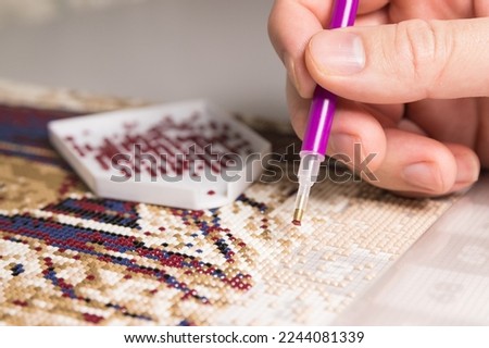 Diamond painting with pen closeup. art therapy concept. Laying out a diamond mosaic improves a woman's mental health. It calms and helps to cope with internal tension, worries and anxiety. Royalty-Free Stock Photo #2244081339