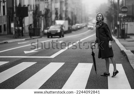 A woman with an umbrella crossing the street in the fog. Black and white photograph.