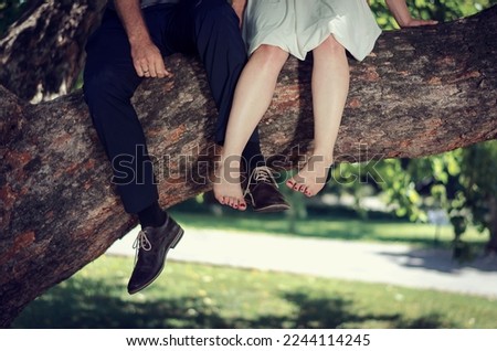 Nicely dressed gentleman's and barefoot woman's legs while sitting upon tree branch for wedding and other couple photoshoots