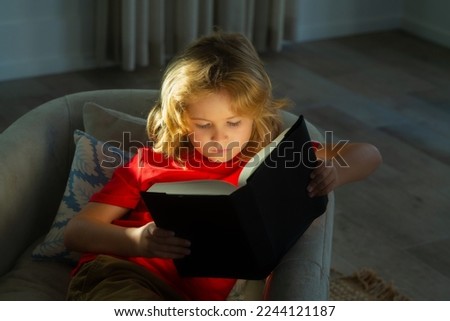 Portrait of cute blonde child reading interesting kids book story. Child reading book at living room. Kids read books. Little boy sitting on couch in sunny living room watching pictures in story book.