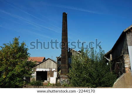 Outdoor view of an abandoned factory, showing a broken brick smokestack