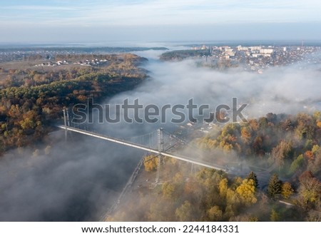 bridge across the river in the autumn morning dense fog over the river. Drone photo. Trees are yellow