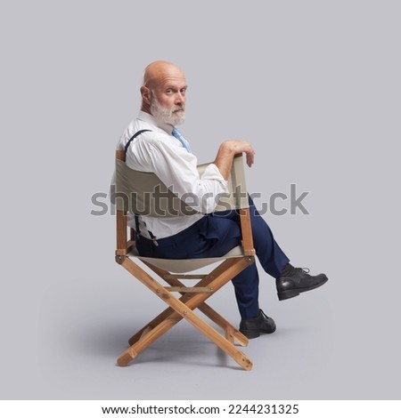 Confident film director sitting on the director's chair and looking at camera: video production, filmmaking and film industry concept Royalty-Free Stock Photo #2244231325