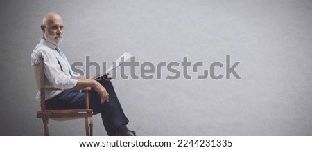 Professional filmmaker sitting on the director's chair and holding a screenplay, he is looking at camera Royalty-Free Stock Photo #2244231335