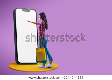 Happy woman doing online shopping using a big smartphone, she is holding shopping bags and touching the blank screen Royalty-Free Stock Photo #2244244915