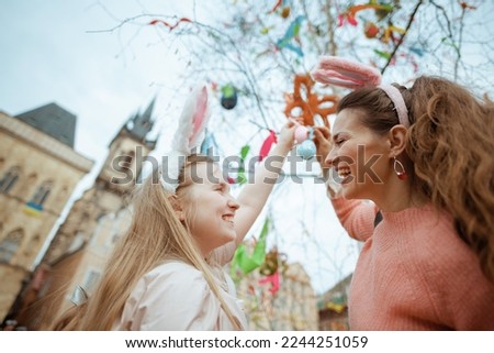 Easter fun. happy modern mother and teenage daughter with easter eggs in the front of easter decorated tree at the fair in the city. Royalty-Free Stock Photo #2244251059
