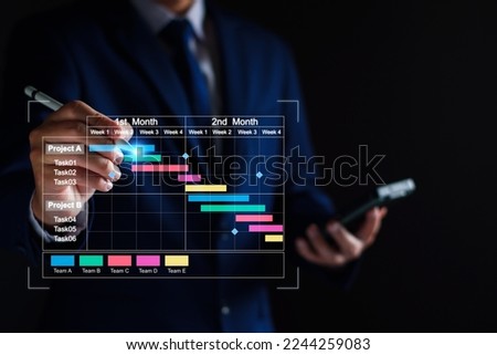 Project manager working on tablet and updating tasks and milestones progress planning with Gantt chart scheduling interface for company on virtual screen. Business Project Management System. Royalty-Free Stock Photo #2244259083