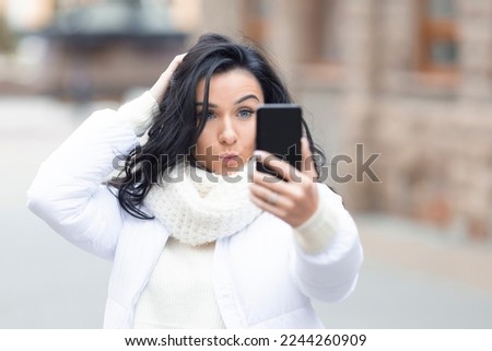 A beautiful young woman makes a funny face to send to friends on social networks in winter.