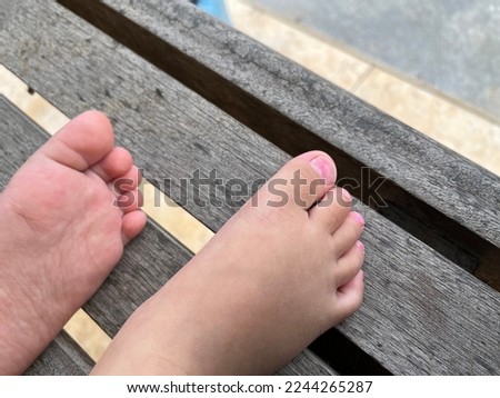 Closeup of little kid sitting and swing on sunny countryside background. Picture of pink toenails children legs barefoot.
