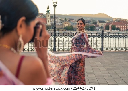 Women tourists in an European capital taking pictures of each other with a vintage camera. Girls with typical Indian clothes do modeling