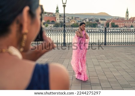 Women tourists in an European capital taking pictures of each other with a vintage camera. Girls with typical Indian clothes do modeling